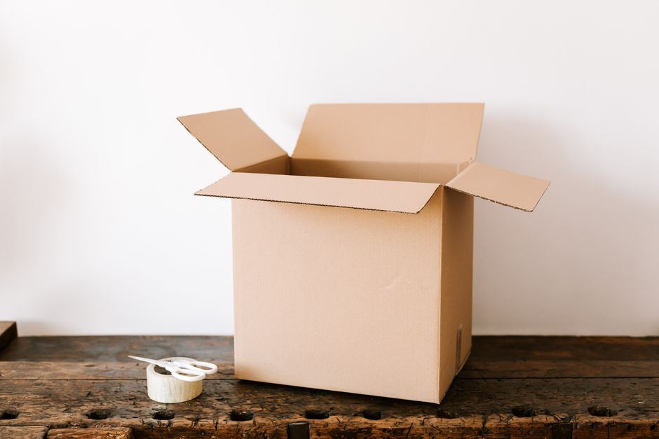 An open corrugated shipping box beside a roll of tape