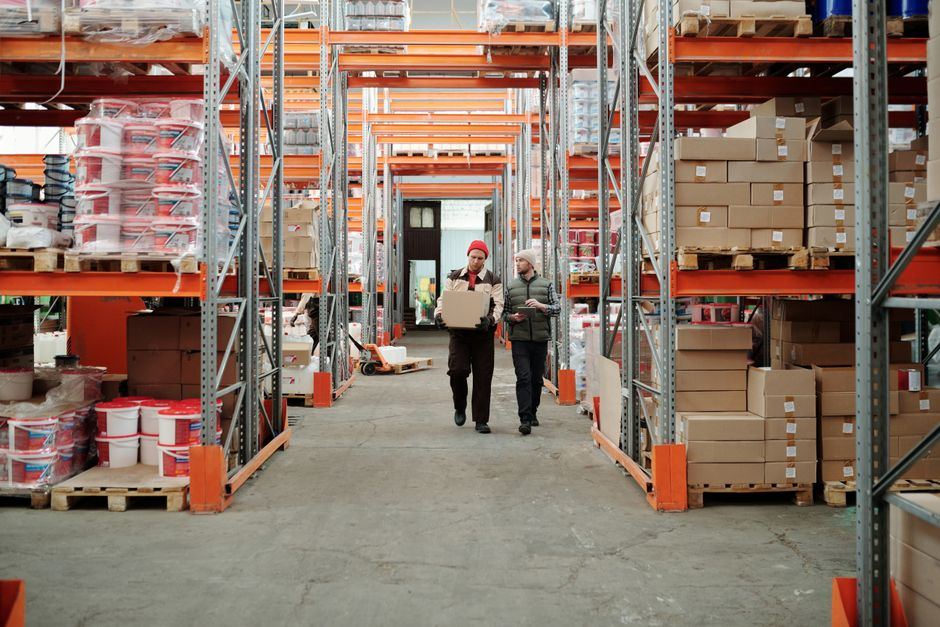 Two people walking down a warehouse aisle with racks of cartons